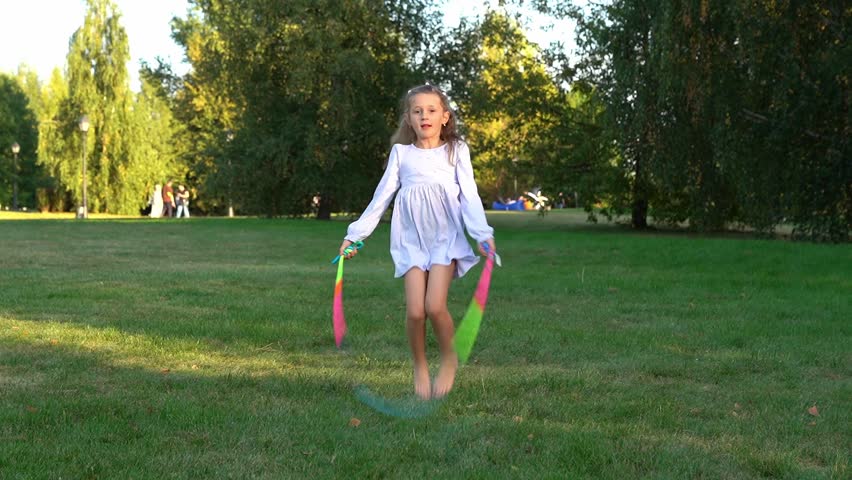 Happy girl jumps rope and laughs in summer park at sunset. Children play in nature. Kids leisure outdoors. Playground