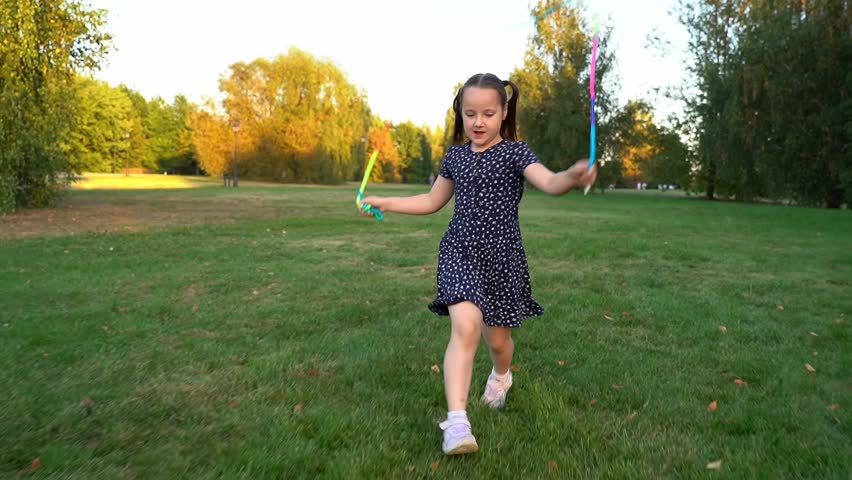 Happy laughing girl runs and jumps rope in summer park at sunset. Children play in nature. Kids leisure outdoors. Playground