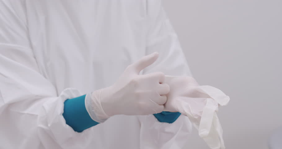 asian female dentist wears protective white uniform and slowly puts on latex gloves before starting dental procedure preparing for oral examination in clinical sterile treatment environment