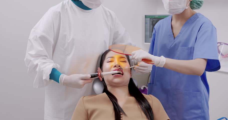 asian female dentist and assistant working together preparing composite resin filling for asian female adult patient during oral treatment using dental curing light and dental mirror