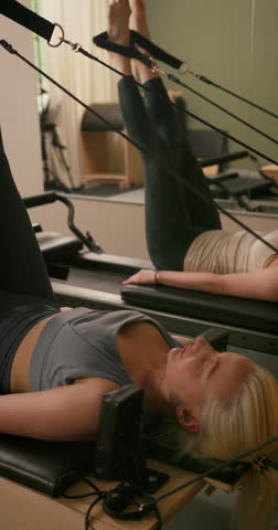 Group of Woman Doing Pilates Exercise on Pilates Reformer for the Chest and Back Muscles, Focusing on Flexibility, Strength, and Control with Determination. Pilates Instructor Helping. Vertical video
