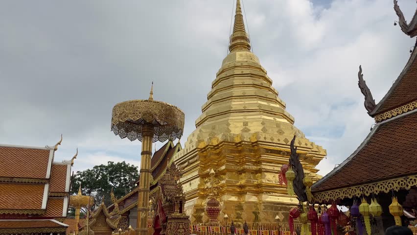 Golden pagoda at Wat Phra Singh, a significant Buddhist temple in Chiang Mai, Thailand. The ornate architecture and cloudy sky create a serene atmosphere.