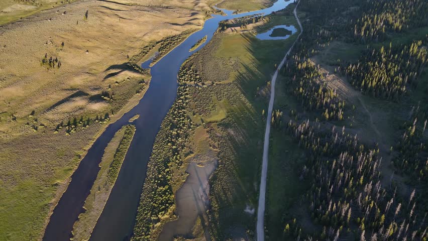 Aerial drone shows winding river flowing through green valley into large lake between tall forest and rocky mountain in scenic peaceful West Virginia landscape under clear blue sky in daylight