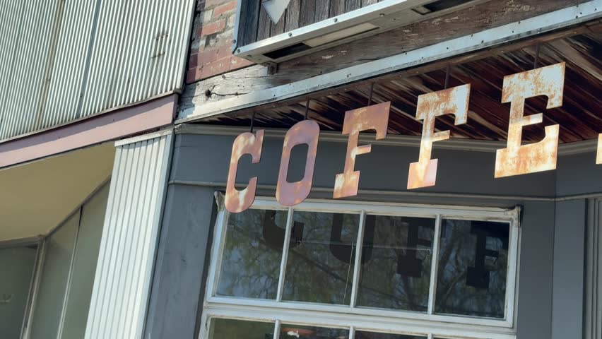 Rustic, rusting coffee cafe sign hanging above the entrance of a ghost town store - isolated street view and panning reveal