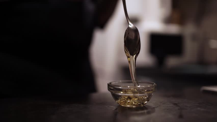 Pouring Golden Honey from Spoon into Glass Bowl Close-Up