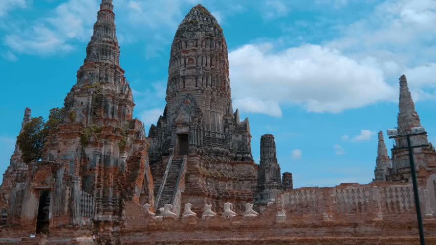 Outstanding ancient Buddhist temple and stupas made of red terracotta brick spread out in the golden yellow sunburned fields of Wat Chaiwatthanaram, Ayutthaya against the background of the blue sky 