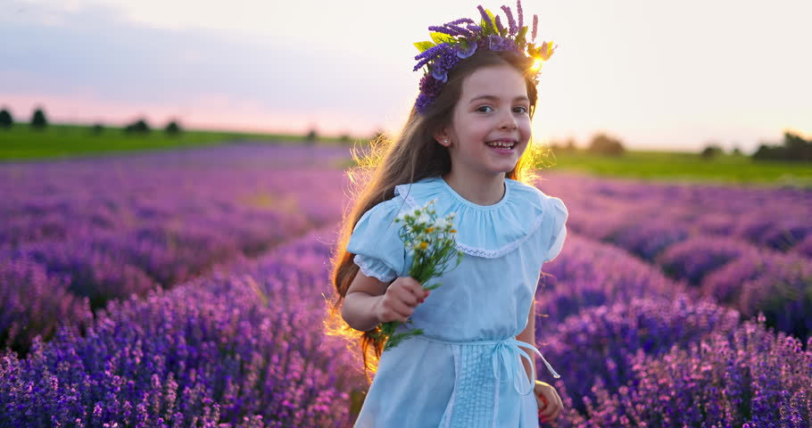 Beautiful bulgarian girl in doll dress, hat, bouquet run on a bloom lavender field with warm sunset light. Bulgaria nature landscape