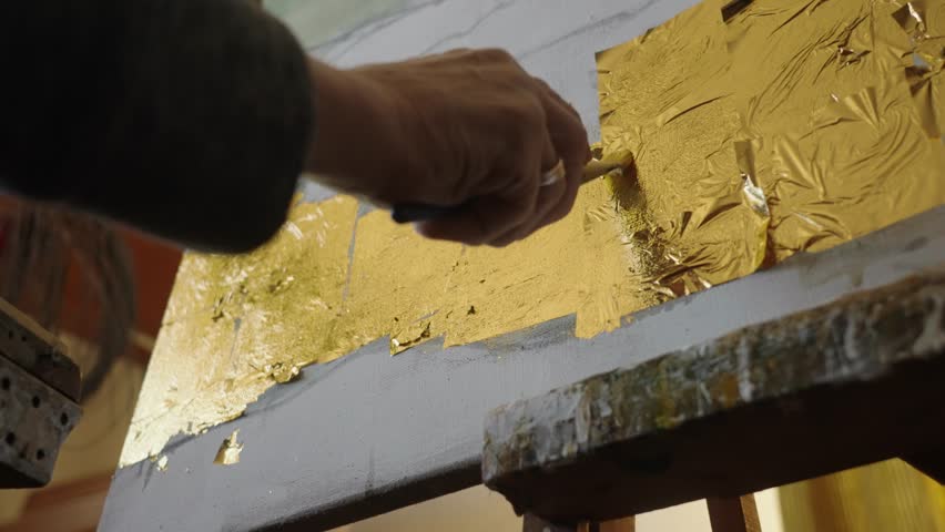 Senior artist on a wheelchair applies gold to the oil painting