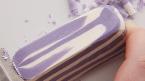 Purple striped soap creates beautiful curling strips as knife peels thin layers producing mesmerizing spiral patterns and therapeutic ASMR sounds on wooden surface creating satisfying experience - Powered by Shutterstock - Get 15% off with code: PIKWIZARD15