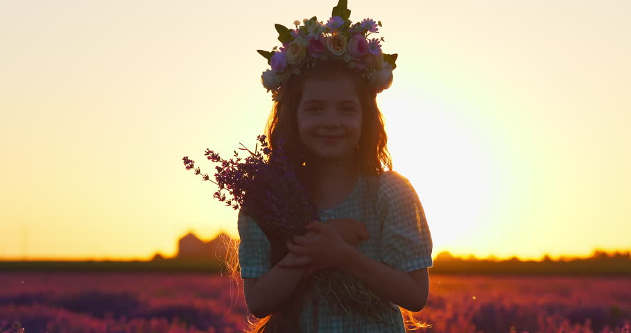 Portrait of beautiful long hair girl with wreath of flowers and bouquet enjoy scenic sunset over blooming lavender field in the countryside