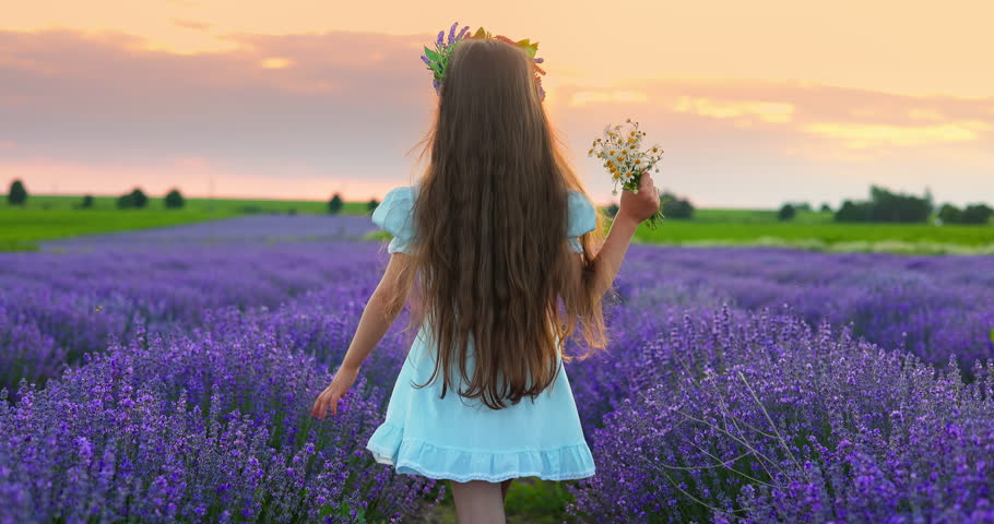 Beautiful bulgarian girl in doll dress, hat, bouquet run on a bloom lavender field with warm sunset light. Bulgaria nature landscape