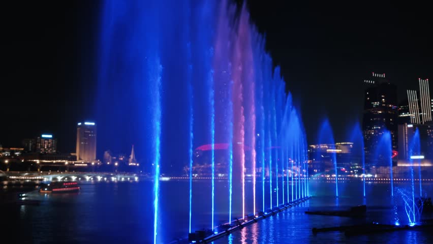 Colorful water show with illuminated fountains and laser lights in front of singapore skyline at night