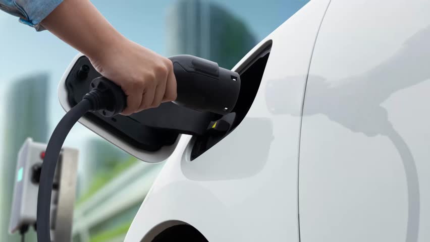 Man insert smart EV charger to electric car and recharging from EV charging station with modern cityscape in background. Futuristic sustainable power and EV car utilization in ESG city. Peruse