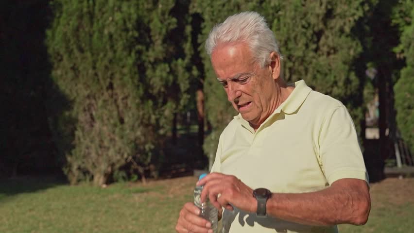 Video of Elderly man drinks water and wipes sweat from his forehead on a hot summer day