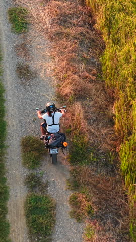 Aerial view of a motorcyclist exploring rural dirt roads between green fields