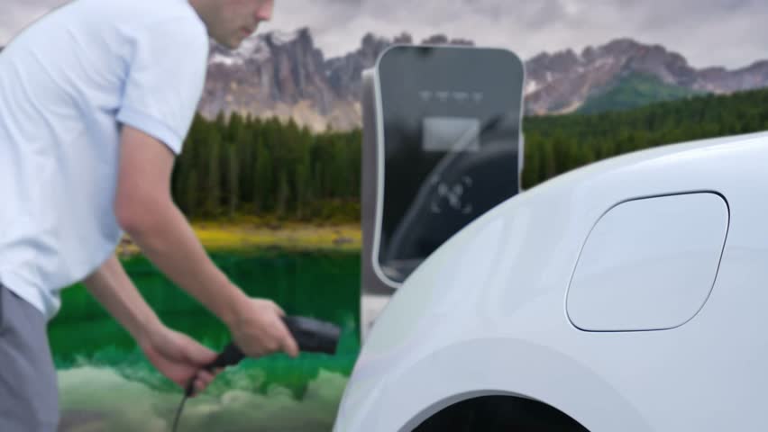 Progressive man charging electric car at the charging point, traveling through nature and mountains in an EV powered by clean and renewable energy for a cleaner environment.