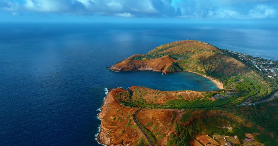 Approaching spectacular Hanauma Bay lit with bright sun. Famous Hawaii landmark at the backdrop of blue waterscape and sky. Aerial view.