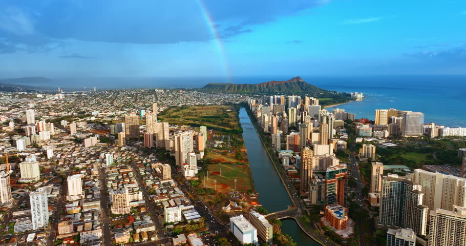 Sunny scenery of Honolulu, Hawaii, USA. Drone footage rising above Ala Wai Canal outlining Waikiki area. Rainbow over the Diamond Head Crater at backdrop.