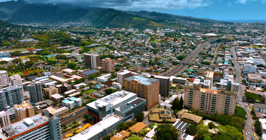 Sunny scenery of Honolulu, Hawaii, USA. Approaching a busy highway crossing the cityscape. Aerial view.