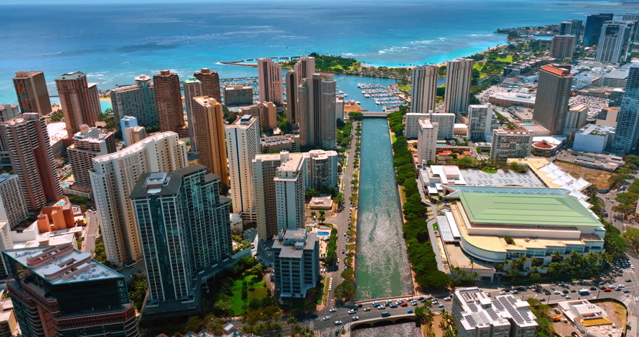 Flight over the sparkling waterscape of the Ala Wai Canal in Honolulu, Hawaii, USA. Pacific Ocean at backdrop. Aerial perspective.
