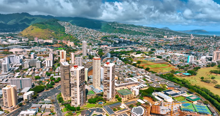Modern lively Honolulu, Hawaii, USA on sunny daytime. Dramatic cloudscape covering the hills at backdrop. Aerial perspective.