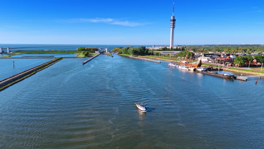 Approaching motor boat on the waterscape of the Markermeer Lake in Lelystad, the Netherlands. Drone footage revealing view on the telecom tower and green cityscape.