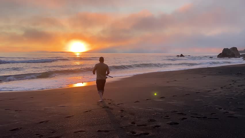 Man fishing from beach during sunset