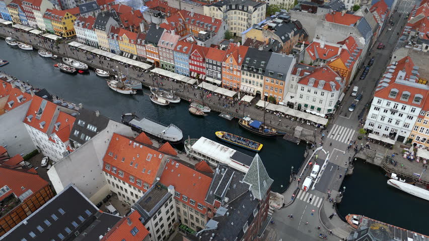 Aerial jib shot of the historic Nyhavn waterfront, a 17th-century canal and entertainment district lined by brightly coloured townhouses, bars and restaurants in Copenhagen, Denmark.