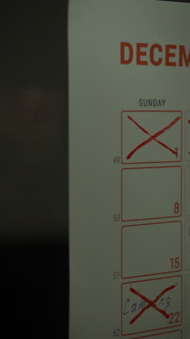 A white Asian man's hand is placing a sticky note on a weekly planning calendar. The calendar shows days marked for organization and goal setting, specifically during December