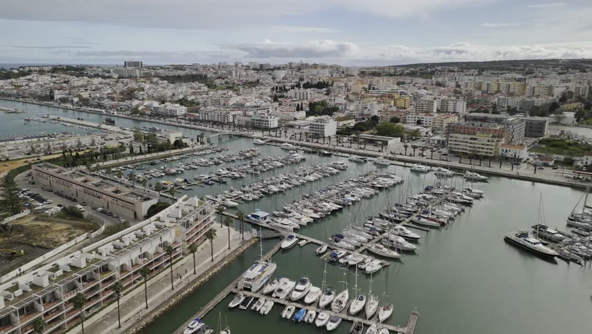 Drone flies to the right over the north side of the boat marina on the Ribeira de Bensafrim on partially cloudy day in Lagos, Portugal