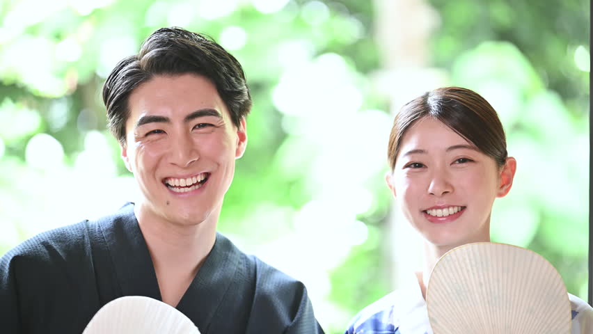 A Japanese couple wearing yukatas stands against a backdrop of fresh greenery. Images of sightseeing and travel. A video with smiling faces looking at the camera.