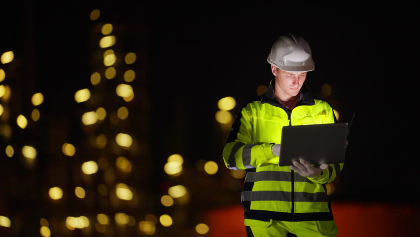 Male petrochemical industry engineer working on laptop computer and inspection petroleum oil refinery plant construction site at night. Industrial technician maintaining energy power gas system.