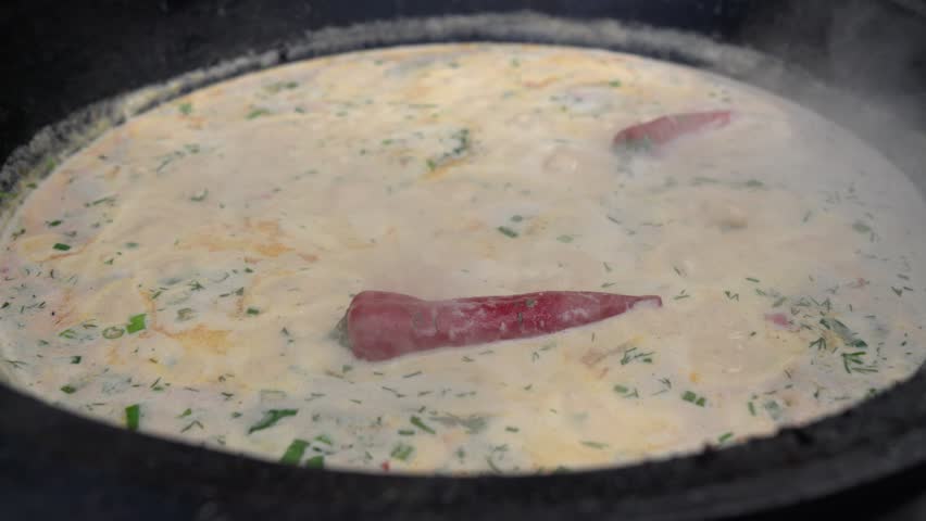 Authentic Finnish fish soup with cream boiling in a cast iron pot. Colored with green and red chili peppers. The rustic dish.
