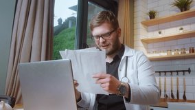 Male doctor in a white coat reviewing medical papers while working from home on a laptop, seated in a bright kitchen. - Powered by Shutterstock - Get 15% off with code: PIKWIZARD15