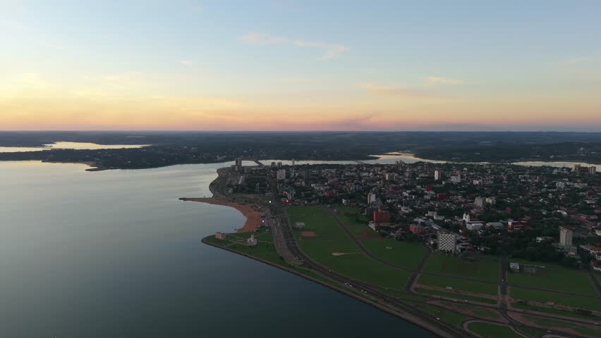 Calm riverside cityscape with curved coastlines under a colorful twilight sky, Encarnación, Itapúa, Paraguay.
