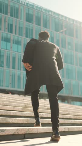 Young black man going up on stone staircase in city, back view, move to goal. Slow motion shot outdoors in downtown, businessman running to office center, be late and motion to dream, career growth