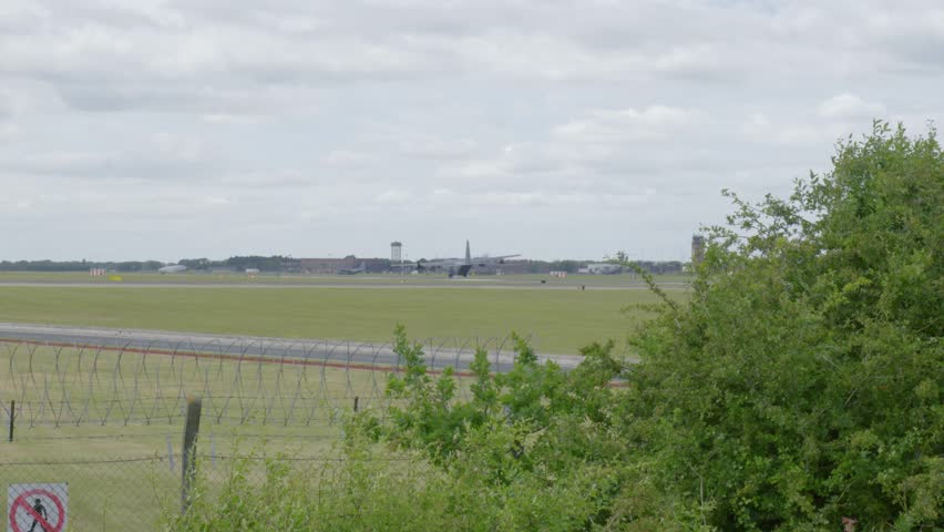 Wide view of RAF Mildenhall runway and base buildings behind barbed wire fence