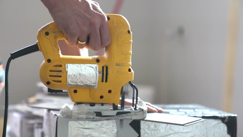 An electric jigsaw cuts quartz vinyl in an apartment. Repair work in the apartment using a saw. Cutting tiles indoors. High quality 4k footage