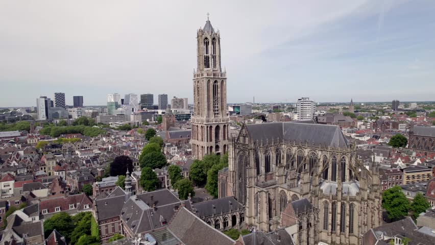 Slow ascending aerial movement showing gothic architecture of cathedral and De Dom church tower in historic city center of Utrecht with Dutch high rise buildings in background