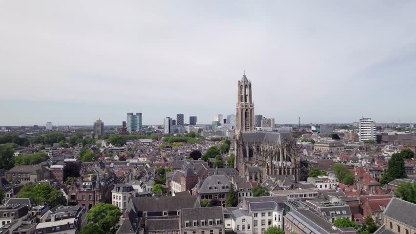 Descending aerial revealing historic city center buildings beneath Utrecht gothic architecture of diocese ambulatory with modern high rise buildings on the horizon behind