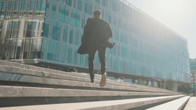 Cinematic shot in urbanscape, man running up of upstairs in business district. Back view of stylish african male person in black coat moving to office building, move to future success, career growth - Powered by Shutterstock - Get 15% off with code: PIKWIZARD15