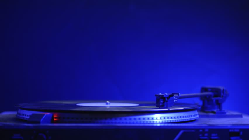 Turntable playing vinyl with colorful lights flashing in the background, perfect retro music party setup in slow motion.