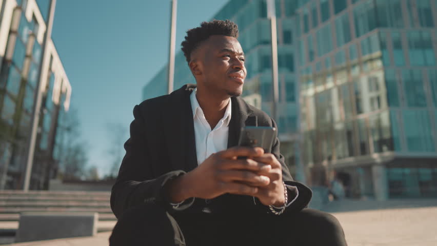 Relax in city, african american businessman sitting alone on street and dreaming . Sad rich man stay lonely, feel yourself abandoned and lonely, black guy with modern smartphone in hands, portrait