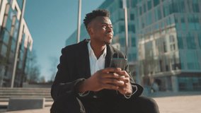 Relax in city, african american businessman sitting alone on street and dreaming . Sad rich man stay lonely, feel yourself abandoned and lonely, black guy with modern smartphone in hands, portrait - Powered by Shutterstock - Get 15% off with code: PIKWIZARD15