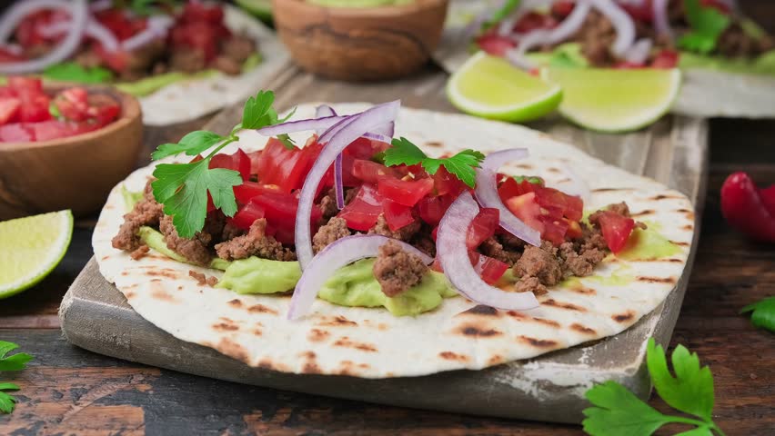 Preparing Beef Tacos with guacamole, tomato, onion and sauce. Tortilla Fast Food