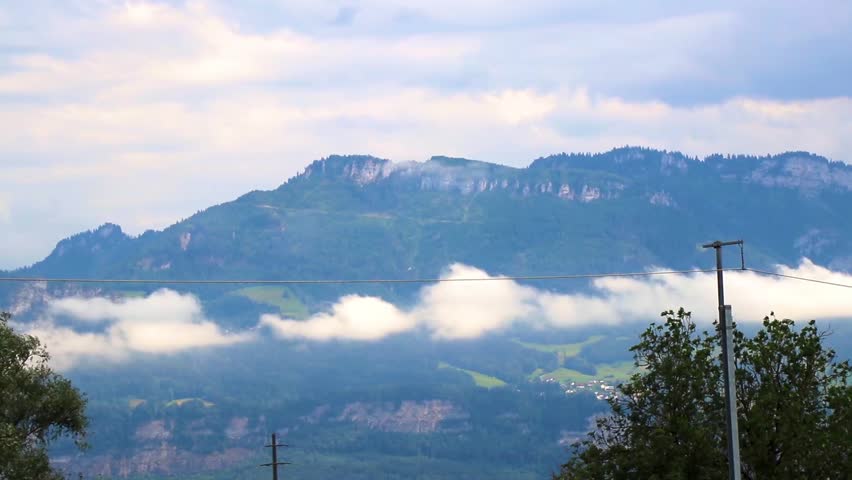 Mountain and alpine hill landscape mountains and peaks with green fields forest nature clouds and blue sky in the Alps Vorarlberg Austria.