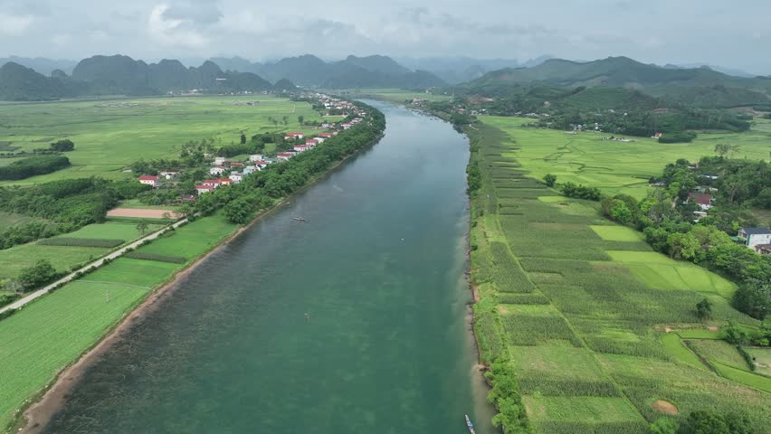 Aerial drone footage flying over the scenic Son River in Quang Binh, Vietnam. The river flows through a lush green valley with agricultural fields and mountains.