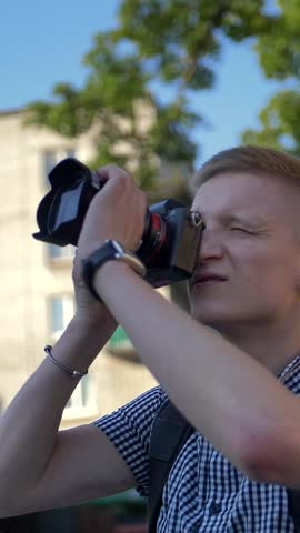 Young student photographer looks at the camera viewfinder to take picture of an interesting attraction. Sunny day. Culture and history interested young man concept. Vertical shot.