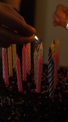 Woman and man lights candles on tasty birthday cake. Prepearing for party. Only hands with Lucifer match. Darkness 4k Ultra HD slow motion footage. Vertical shot.