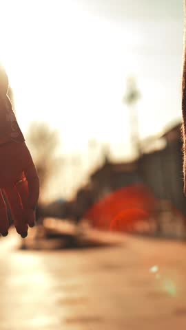 Couple hands holding each other on city street sunset light with beautiful lens flare. Male and female lovers touching their arms. Super slow motion shot. Vertical shot.